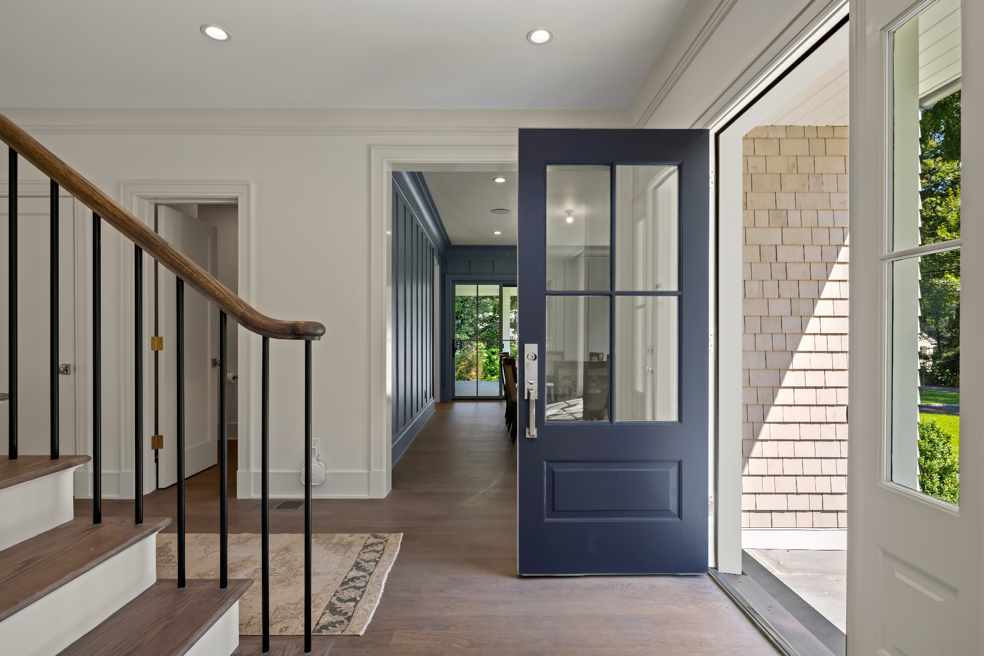 Sunlit entryway of a contemporary home with a navy front door and natural oak flooring